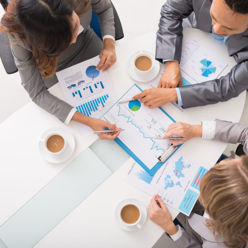 Business executives discussing charts and diagrams at meeting, view from above