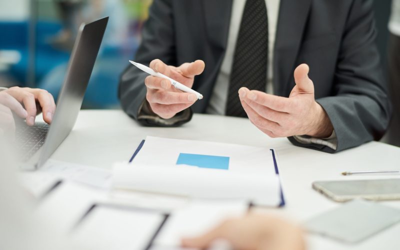 Closeup of unrecognizable businessman holding pen and gesturing actively while talking to partner in meeting, copy space