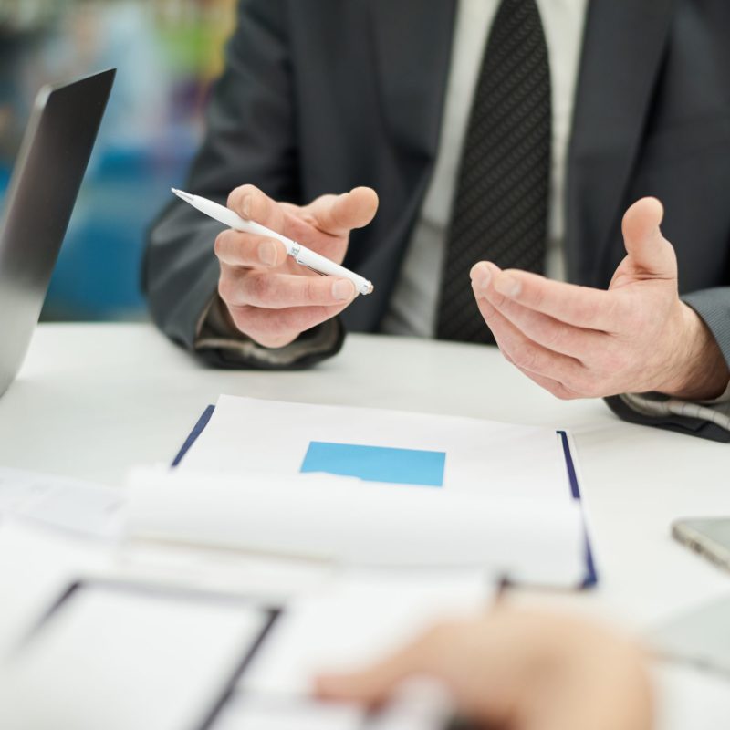 Closeup of unrecognizable businessman holding pen and gesturing actively while talking to partner in meeting, copy space