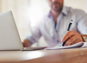 Close up shot of young business man hands with pen writing notes on a paper. Male executive sitting at table at home office.